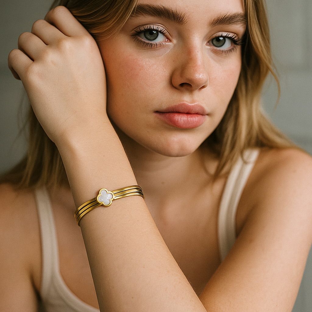 Woman wearing a gold bracelet with a clover-shaped charm on a neutral background
