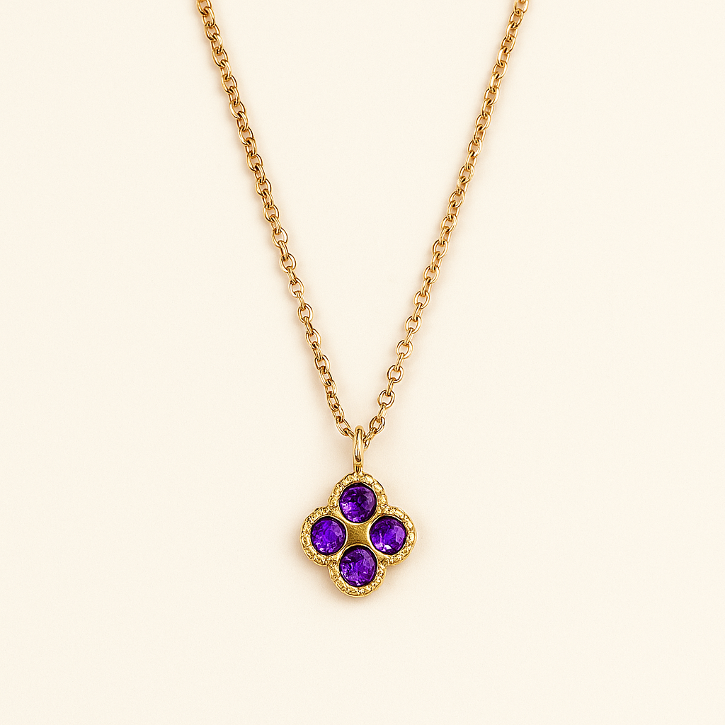 Gold necklace with a clover-shaped pendant featuring purple gemstones on a beige background
