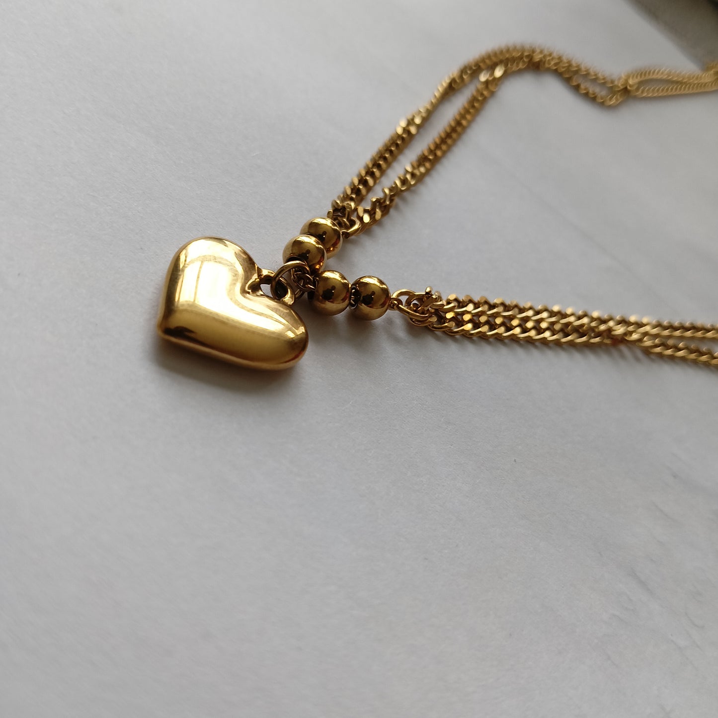 Gold heart-shaped pendant on a chain against a light gray background