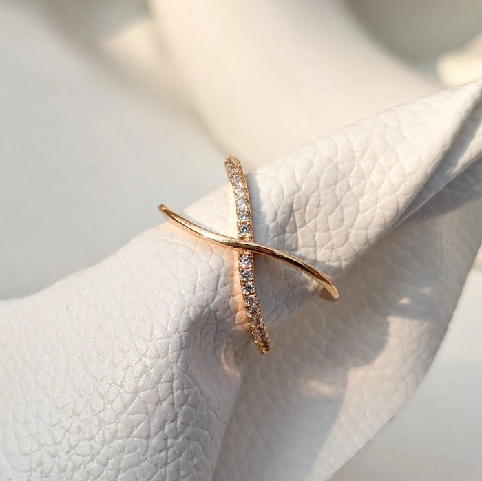A gold-colored ring with a geometric design, featuring what appears to be small gemstones or embellishments, displayed on a white fabric surface.