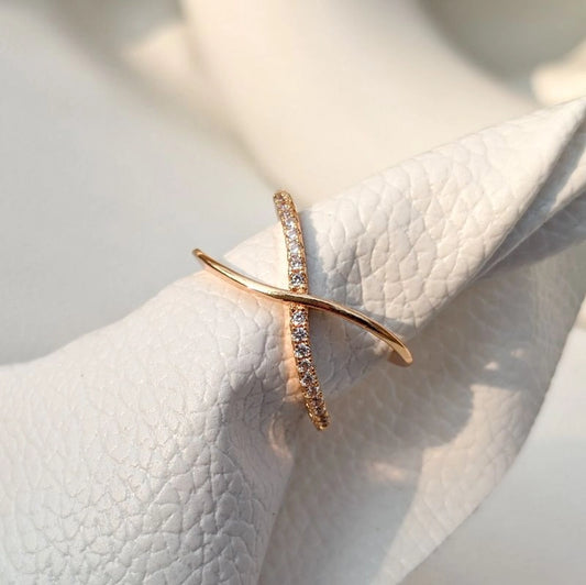 A gold-colored ring with a geometric design, featuring what appears to be small gemstones or embellishments, displayed on a white fabric surface.
