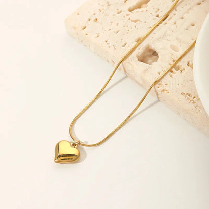A 18K gold heart-shaped pendant necklace placed on a textured surface.