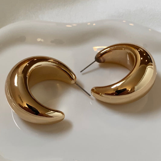 A pair of chunky gold-colored hoop earrings on a white surface.