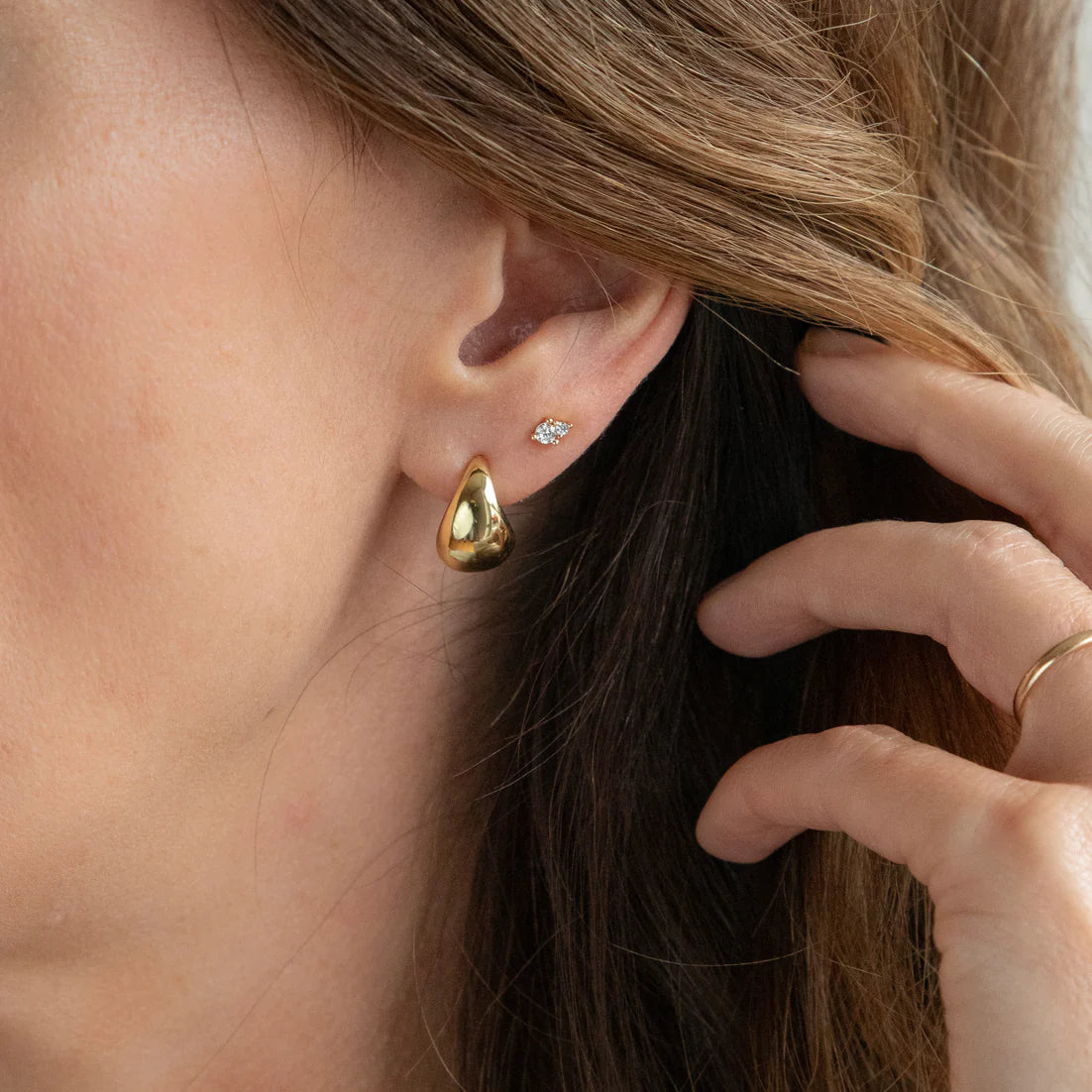 A close-up image of a woman's ear wearing a gold stud earring with a teardrop shape.