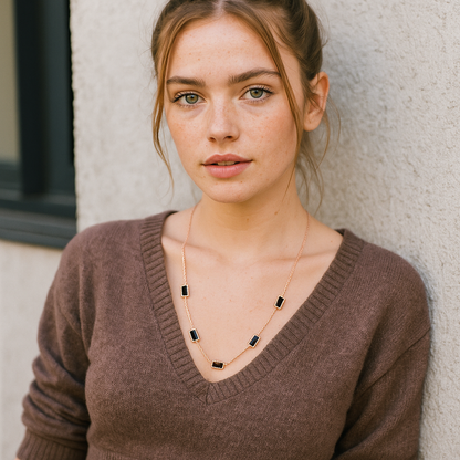 Woman wearing a brown sweater and gold necklace against a neutral background