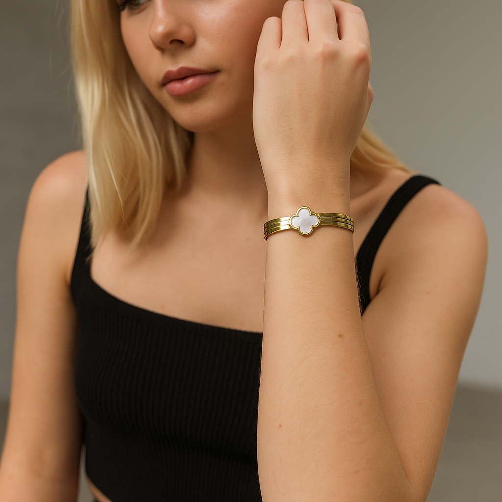 Woman wearing a gold bracelet with a white flower design on a neutral background
