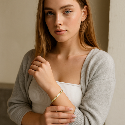 Woman wearing a 18K gold bracelet, wearing a light gray sweater over a white top.