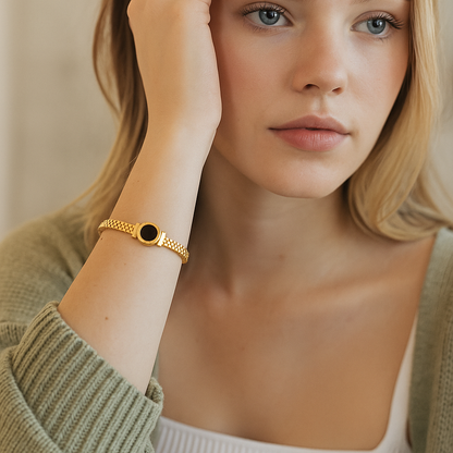 Woman wearing a gold bracelet with a black stone on a neutral background