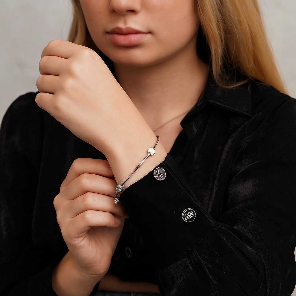 Person wearing a charms and ball silver bracelet with a neutral background