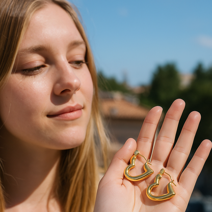 Woman holding gold heart-shaped earrings with a blurred outdoor background