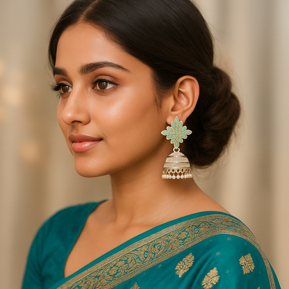 Woman wearing a teal saree with gold patterns and floral earrings against a neutral background