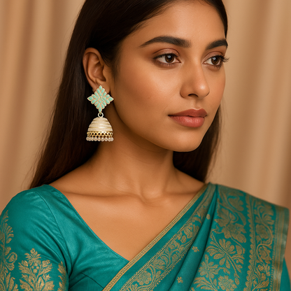 Woman wearing a teal saree with gold patterns and earrings against a beige background