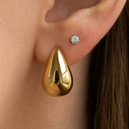 Gold teardrop earring worn on an ear with a blurred background