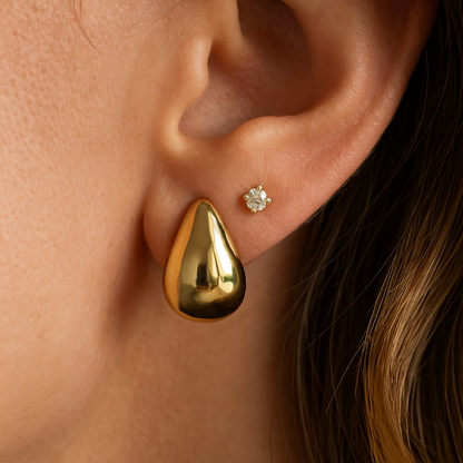 Close-up of an ear wearing a gold teardrop earring and a small diamond earring.