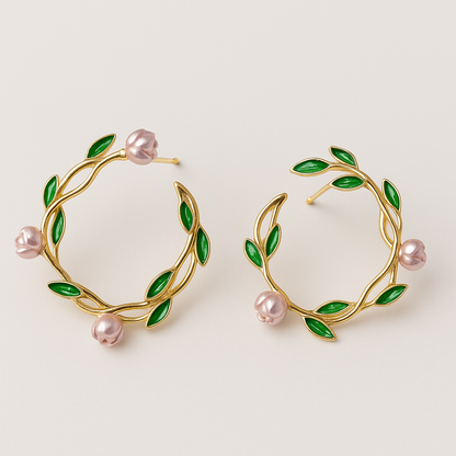 Gold hoop earrings with green leaves and pink pearls on a light beige background