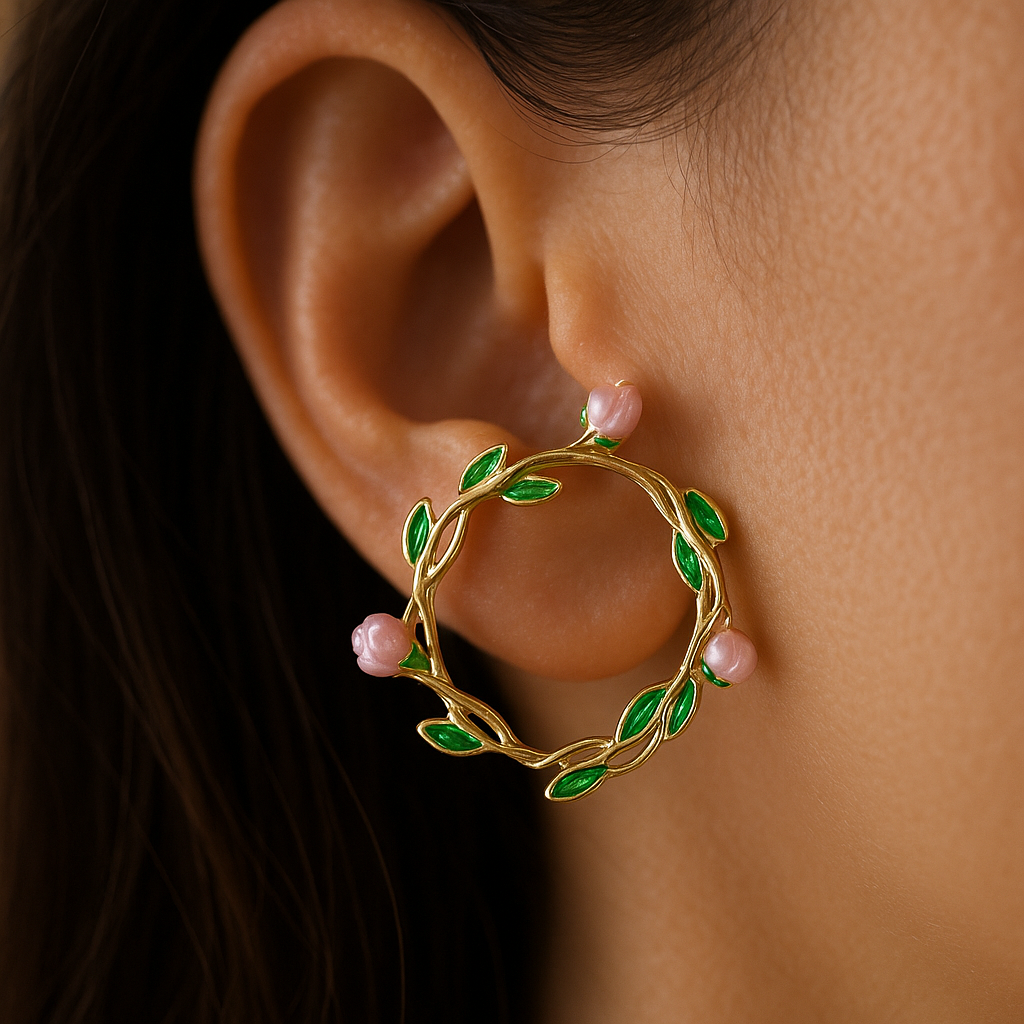 Gold hoop earring with green leaves and pink stones worn by a person.