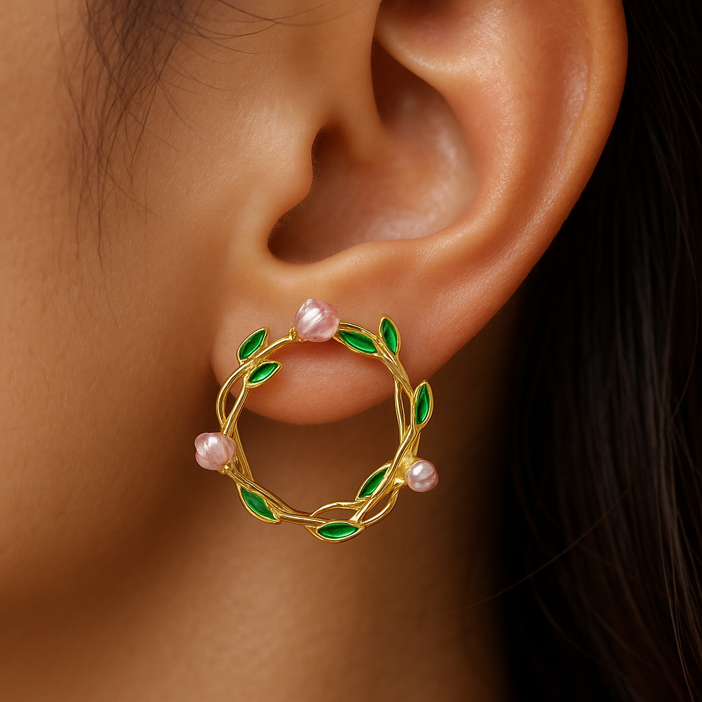 Gold earring with green leaves and pink stones worn by a person