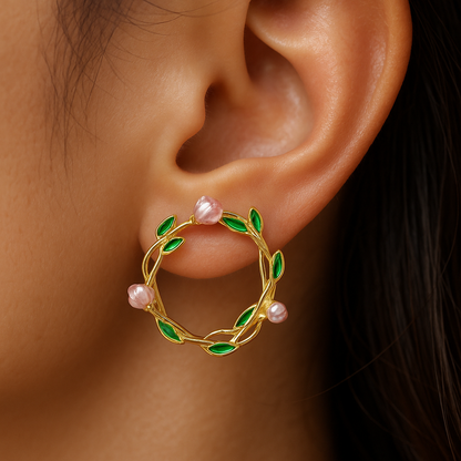 Gold earring with green leaves and pink stones worn by a person