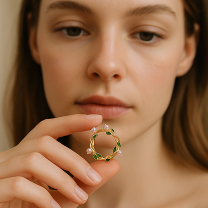 Close-up of a person holding a gold earring with green stones and small pearls.
