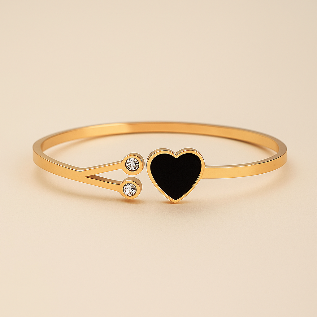 Gold bracelet with a black heart charm on a beige background
