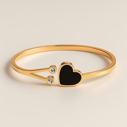 Gold bracelet with a black heart charm on a beige background