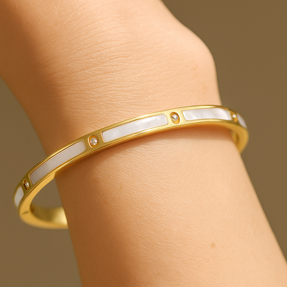 Gold bracelet with white stones on a wrist against a brown background