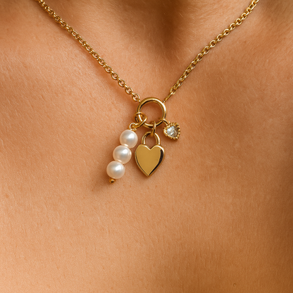 Gold necklace with heart, pearl, and round charm on a person's neck