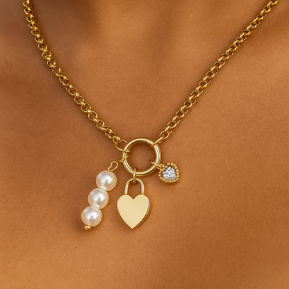 Gold necklace with heart, pearl, and round charm on a brown background