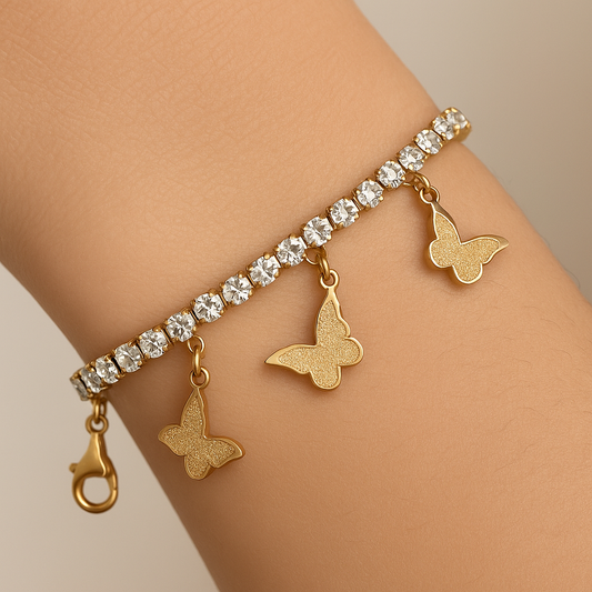 Gold bracelet with butterfly charms and clear stones on a wrist against a neutral background