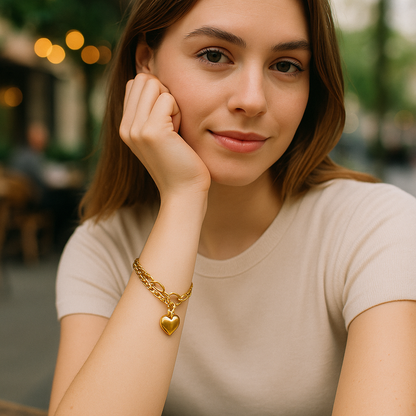 Woman wearing a gold bracelet with a heart charm, sitting outdoors.