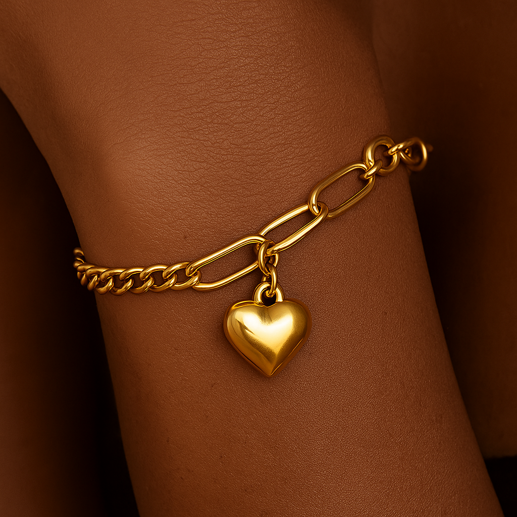 Gold chain bracelet with a heart charm on a wrist against a brown background