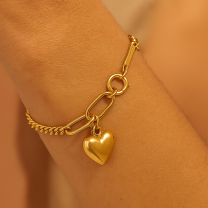 Gold bracelet with a heart charm on a person's wrist against a matching background