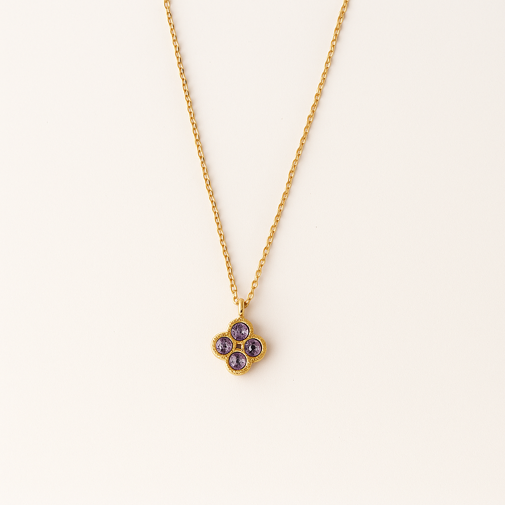 Gold necklace with a purple gemstone pendant on a light beige background
