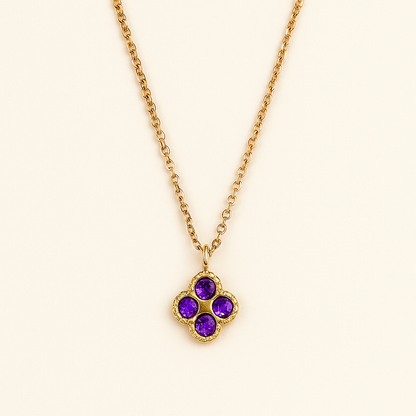 Gold necklace with a clover-shaped pendant featuring purple gemstones on a beige background