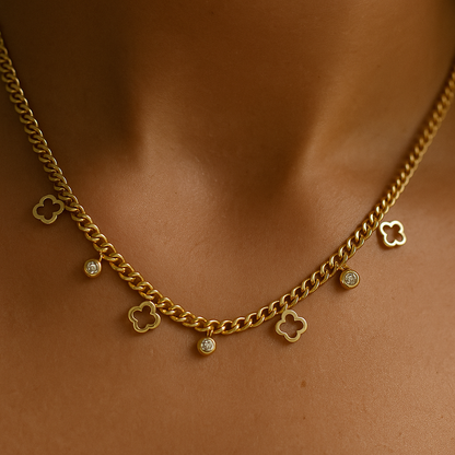 Gold chain necklace with clover-shaped charms on a person's neck against a brown background
