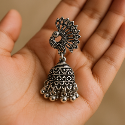 Silver peacock-shaped earring held in a hand against a beige background