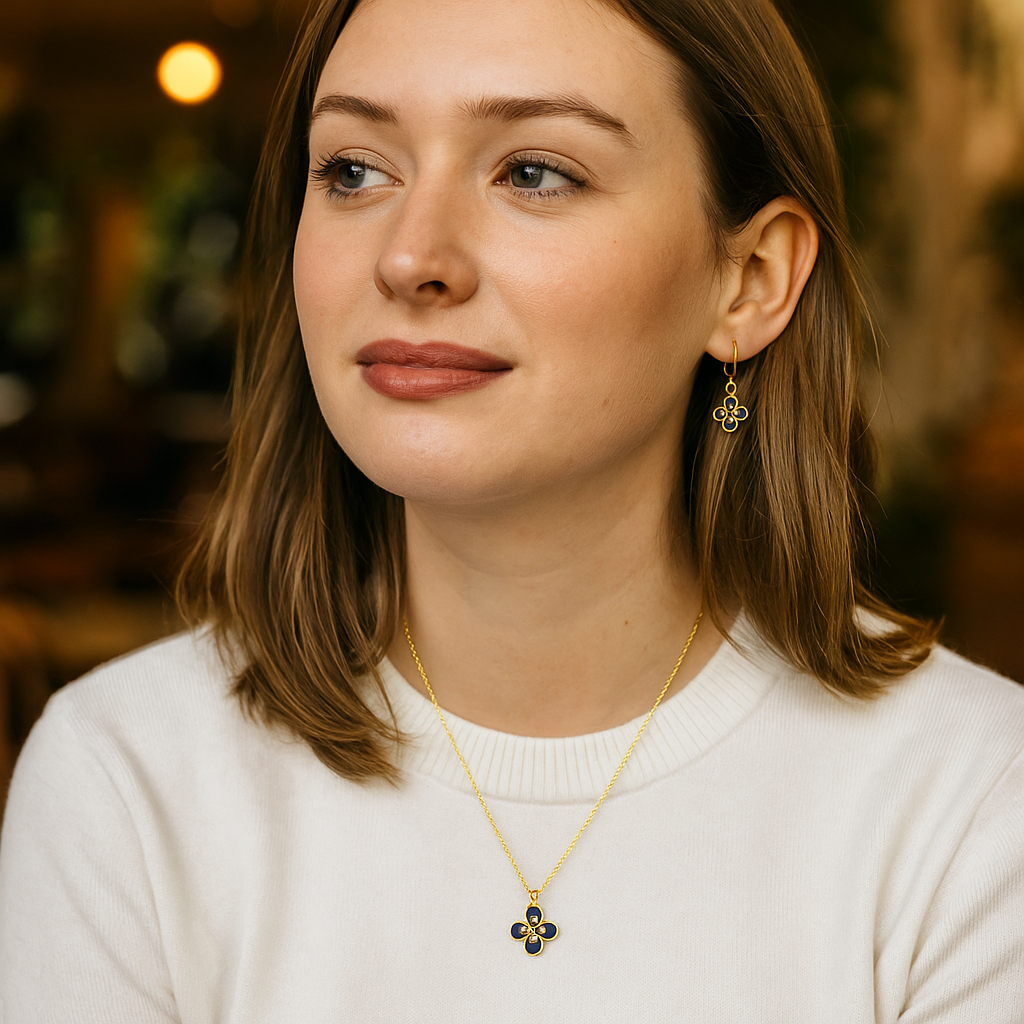 Woman wearing a gold necklace with a pendant, set against a blurred indoor background.