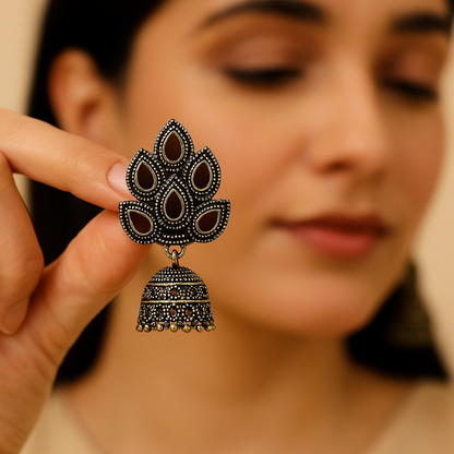 Close-up of a decorative black and gold earring held by a person with a blurred background