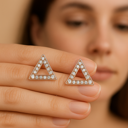 Triangle-shaped earrings with clear stones held by a hand against a blurred background