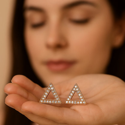 Person holding triangle-shaped earrings with a blurred background
