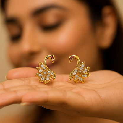Gold swan earrings with diamond details held in a hand against a blurred background