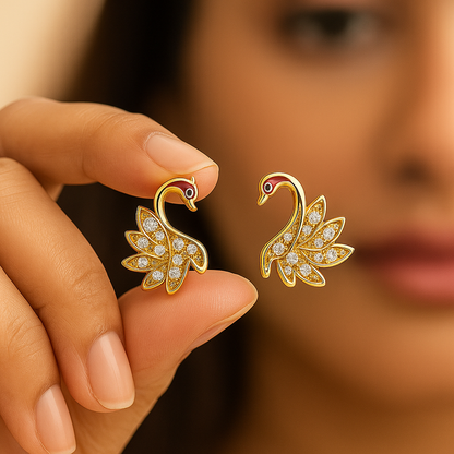 Gold Swan earrings held by a hand with a blurred background