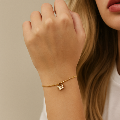 Gold bracelet with a butterfly charm on a wrist against a neutral background