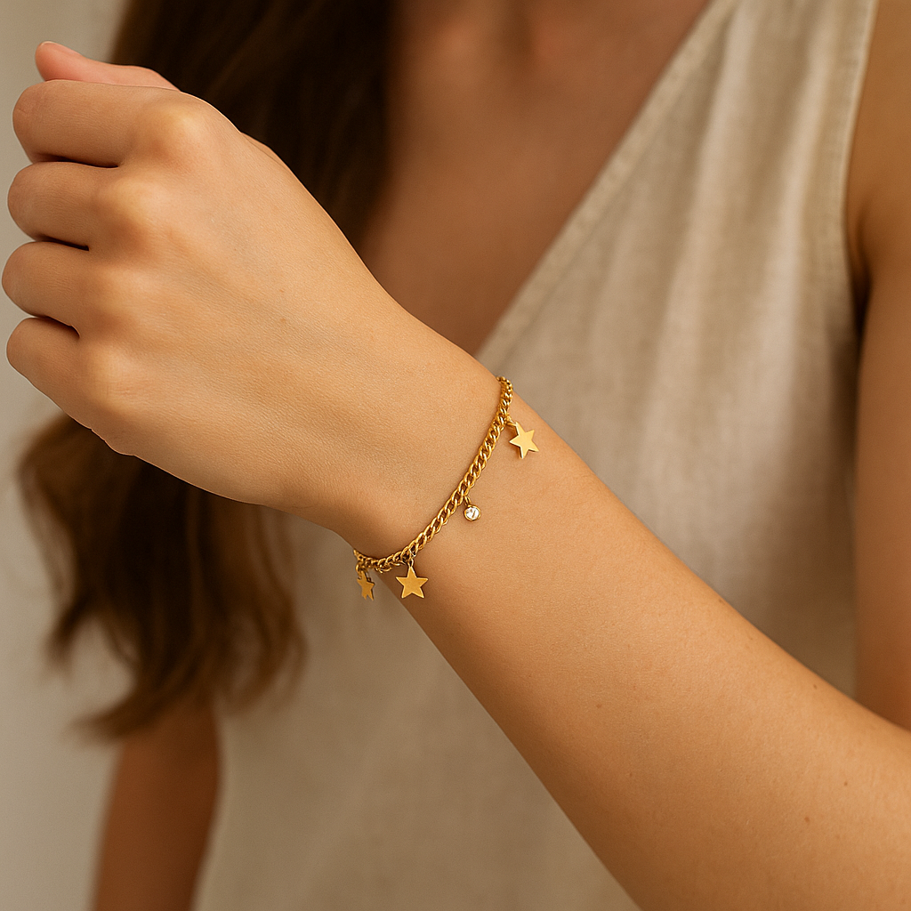 Gold bracelet with star charms on a wrist against a neutral background