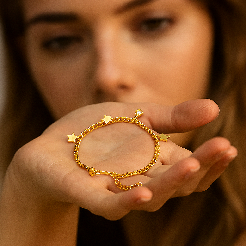 Gold bracelet with star and ball charms held in a hand against a blurred background