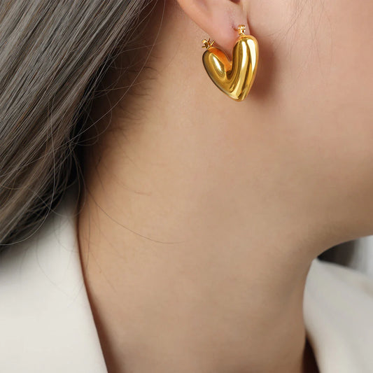 A close-up image of a person wearing 18K gold plated heart-shaped hoop earrings.