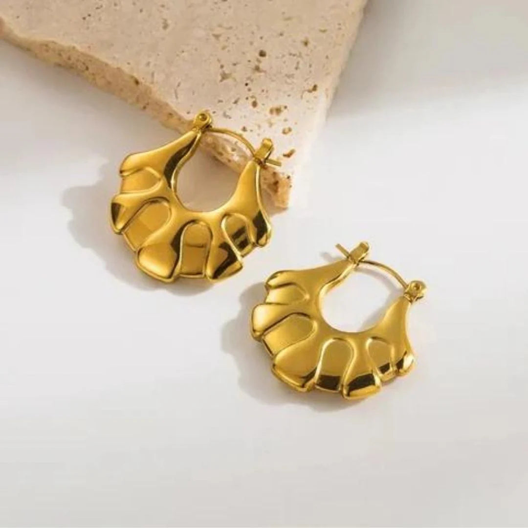 A pair of gold-colored floral hoop earrings resting on a beige surface.