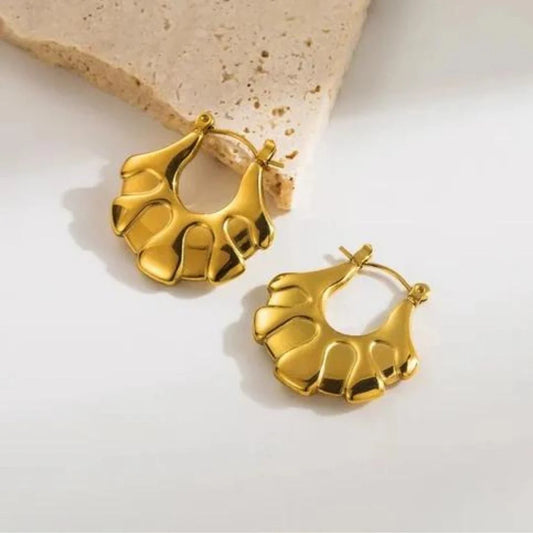 A pair of gold-colored floral hoop earrings resting on a beige surface.