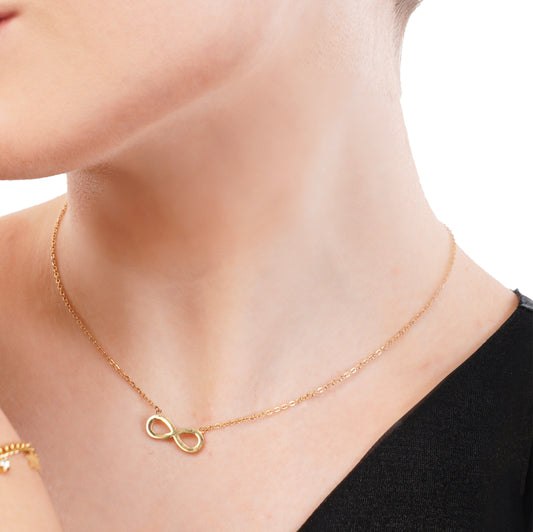 A close-up image of a woman wearing an 18Kt gold infinity chain pendant necklace.