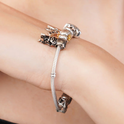 Silver bracelet with charms on a wrist against a neutral background